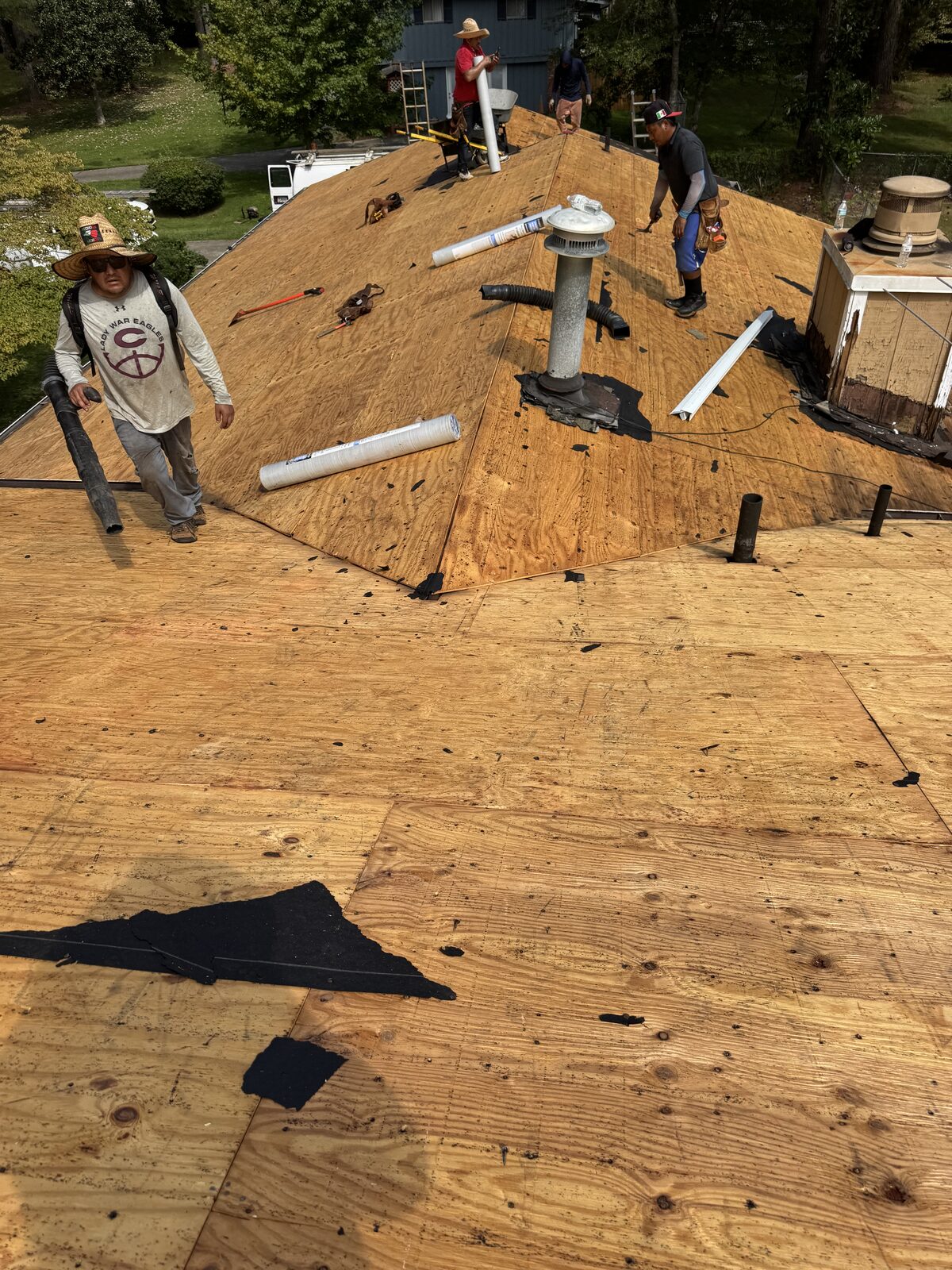 Roofing crew working on new plywood decking and vent pipes